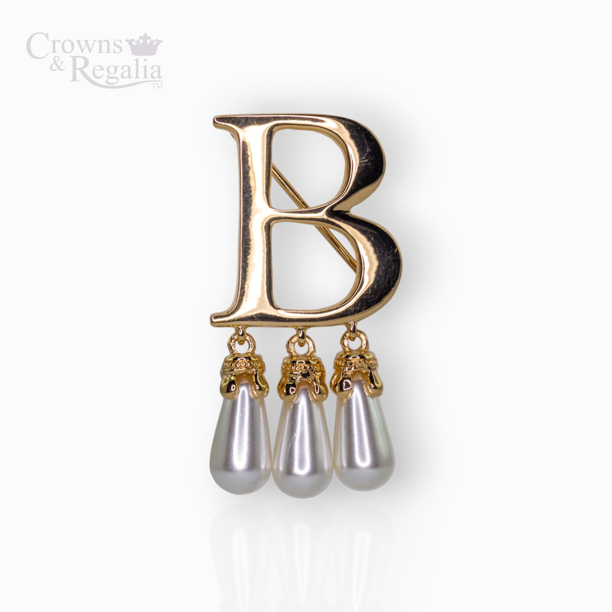 Gold brooch with letter 'B' and pearl-like droplets on a white background, branded 'Crowns & Regalia'.