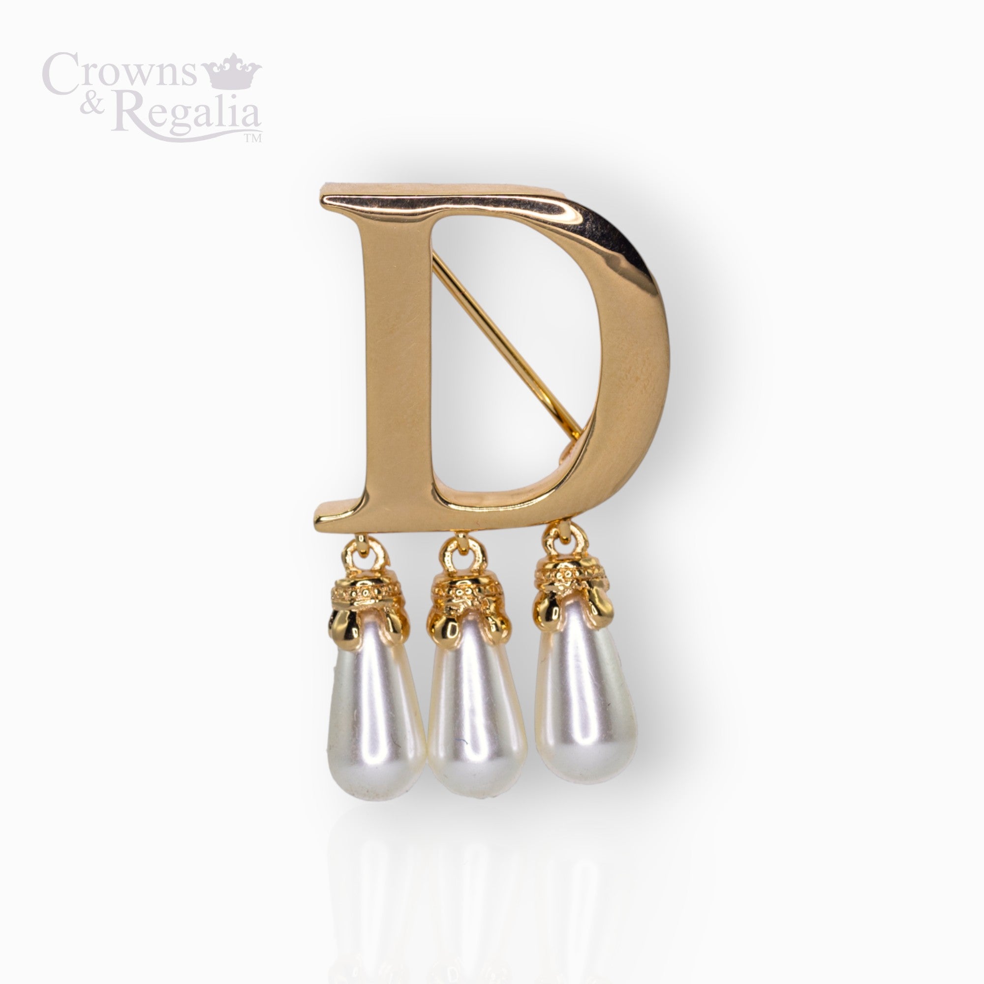Gold brooch with 'D' and pearl-like droplets on a white background, branded 'Crowns & Regalia'.