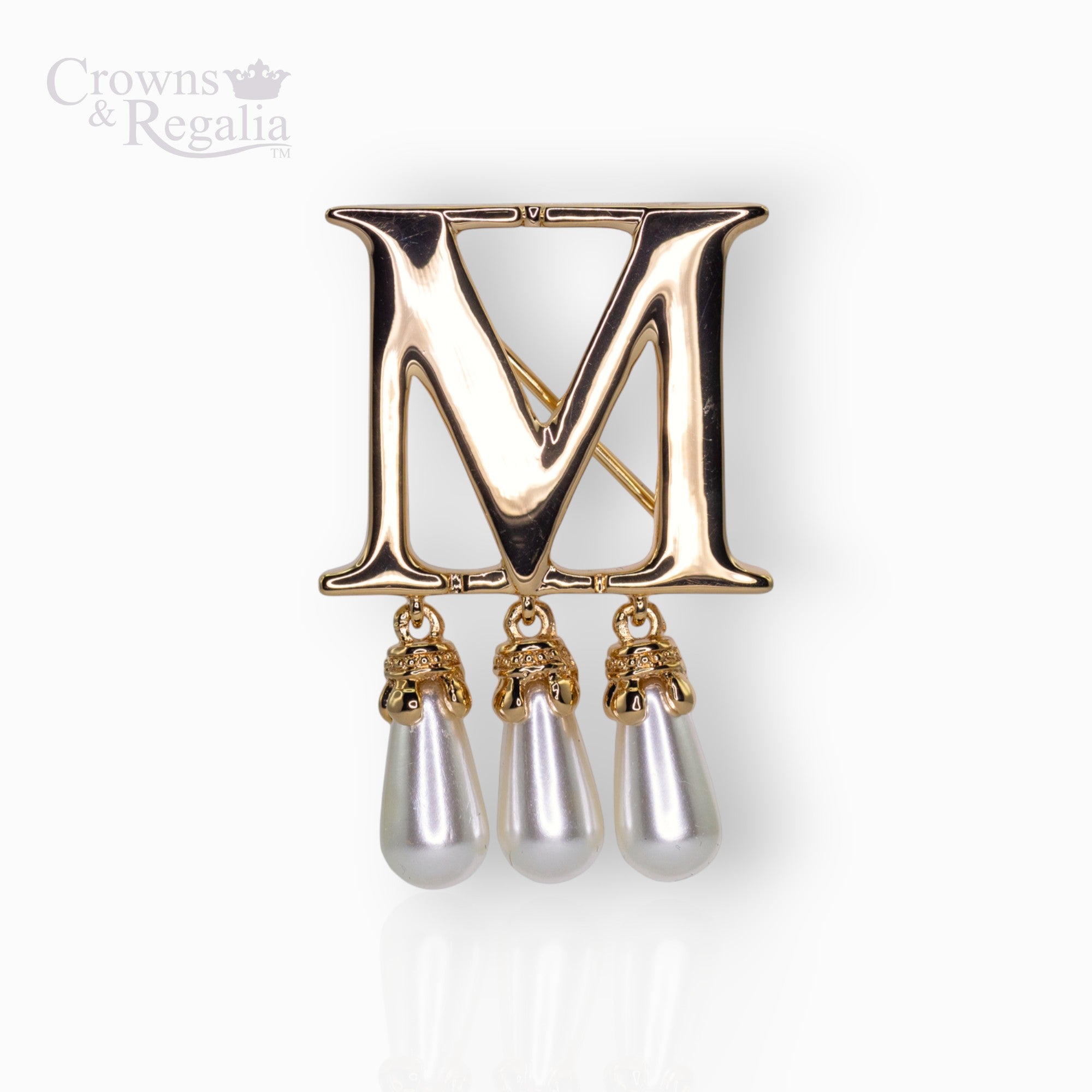 Gold brooch with letter 'M' and pearl-like droplets on a white background, branded 'Crowns & Regalia'.