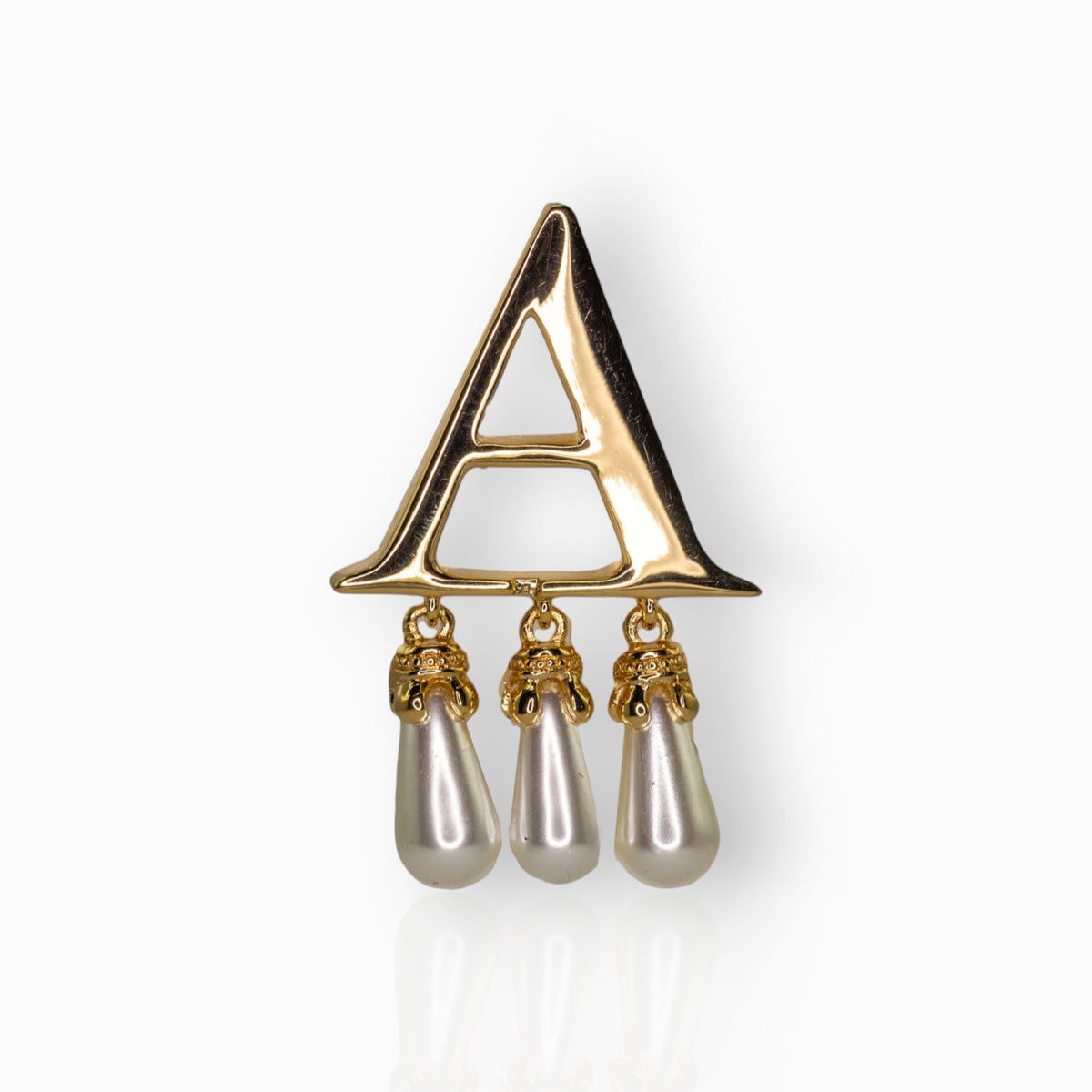 Gold brooch with 'A' and pearl drops on a white background.