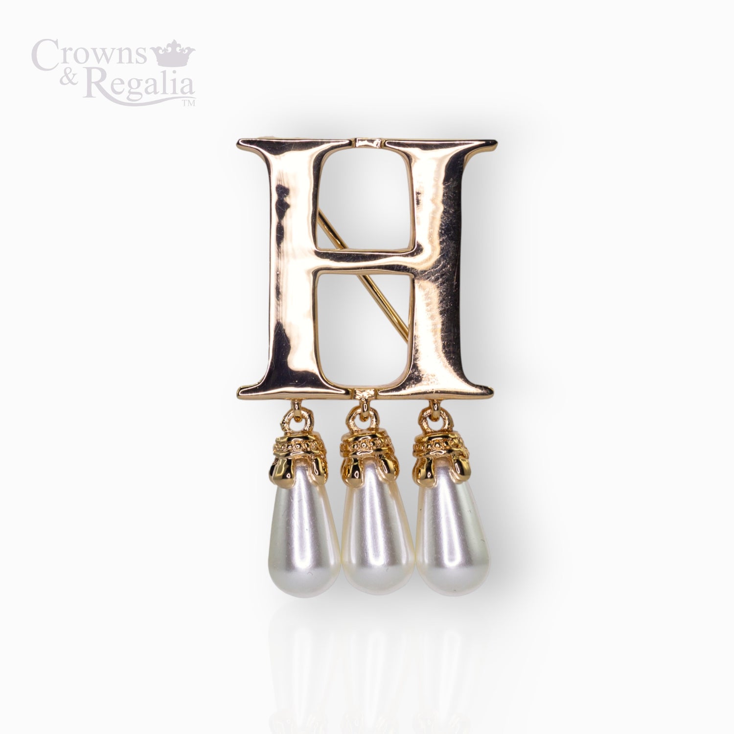 Gold brooch with 'H' and pearl-like droplets on a white background.