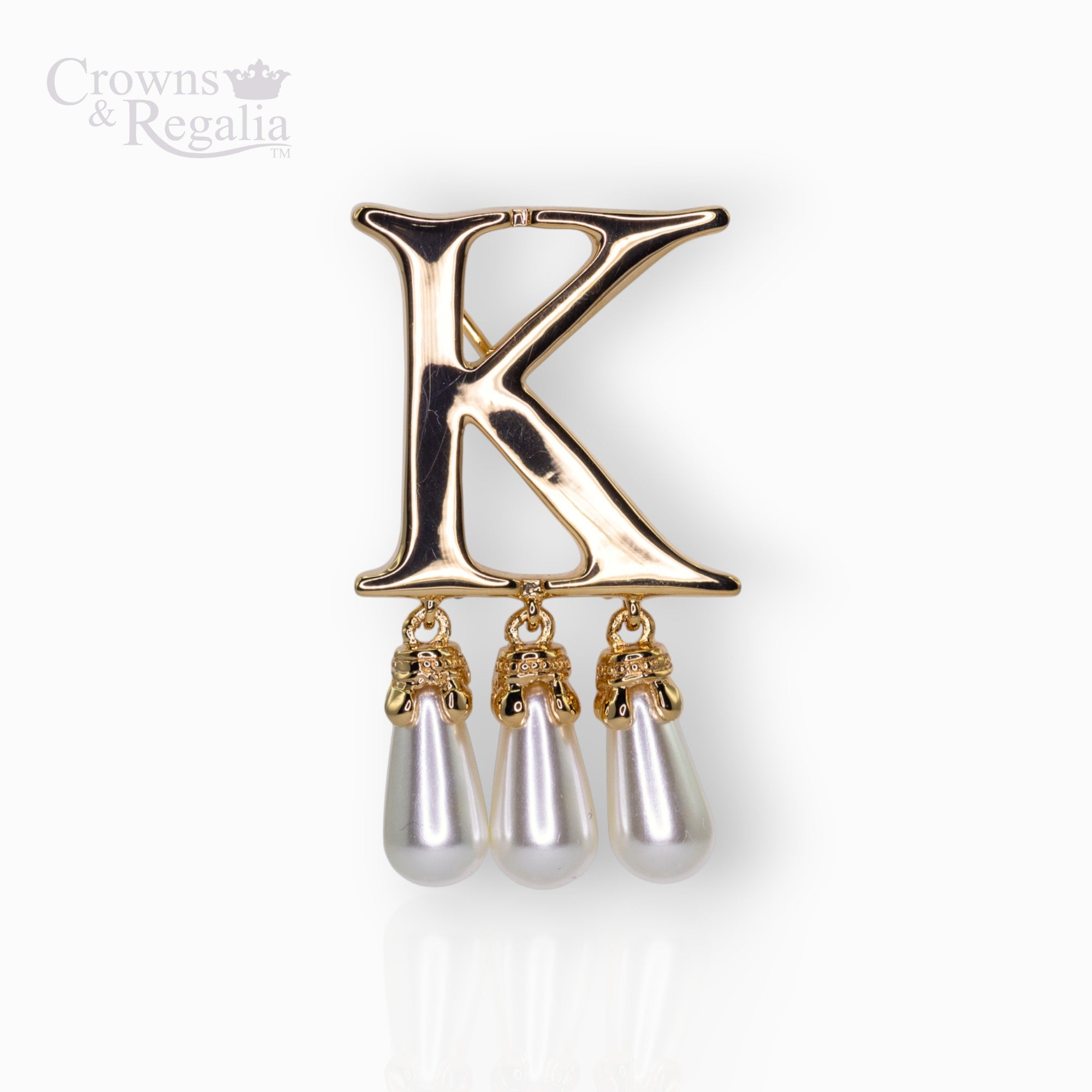 Gold brooch with letter 'K' and pearl-like droplets on a white background, branded 'Crowns & Regalia'.