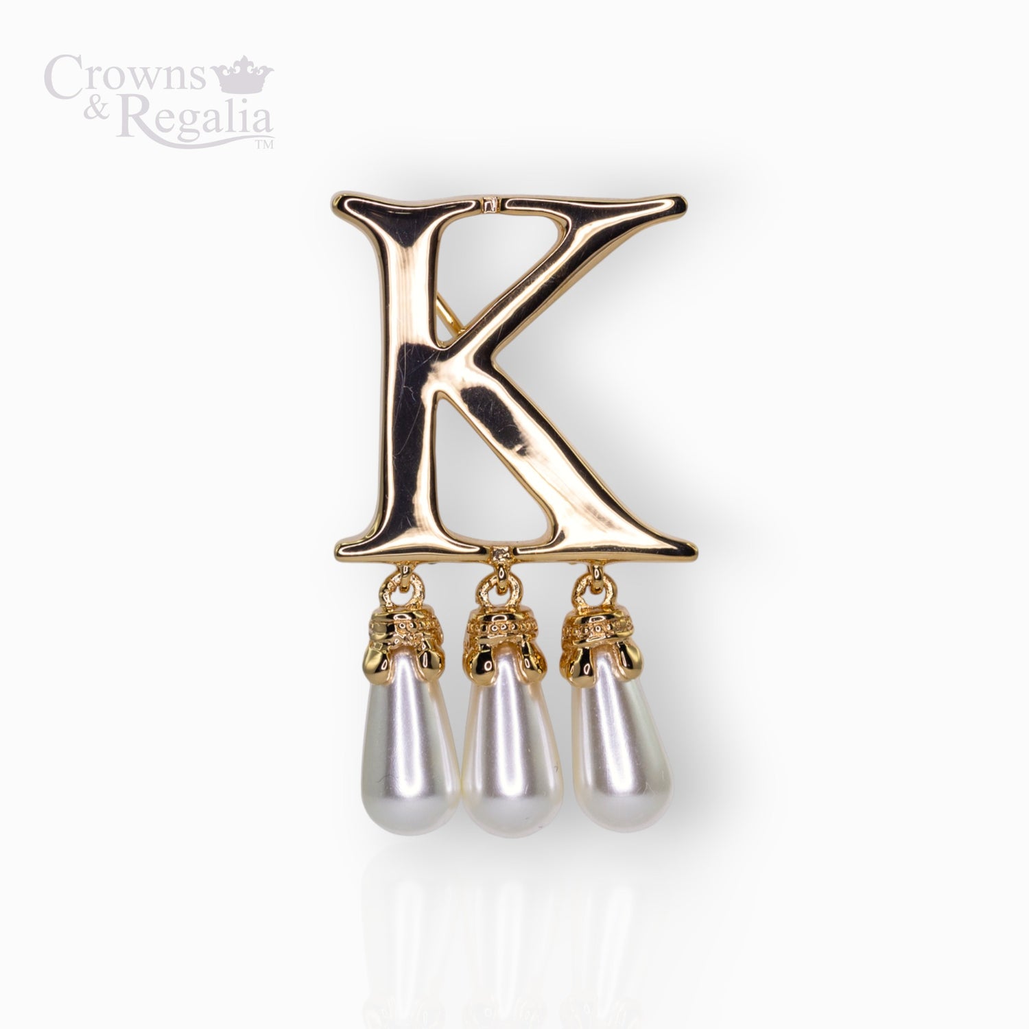 Gold brooch with letter 'K' and pearl-like droplets on a white background.