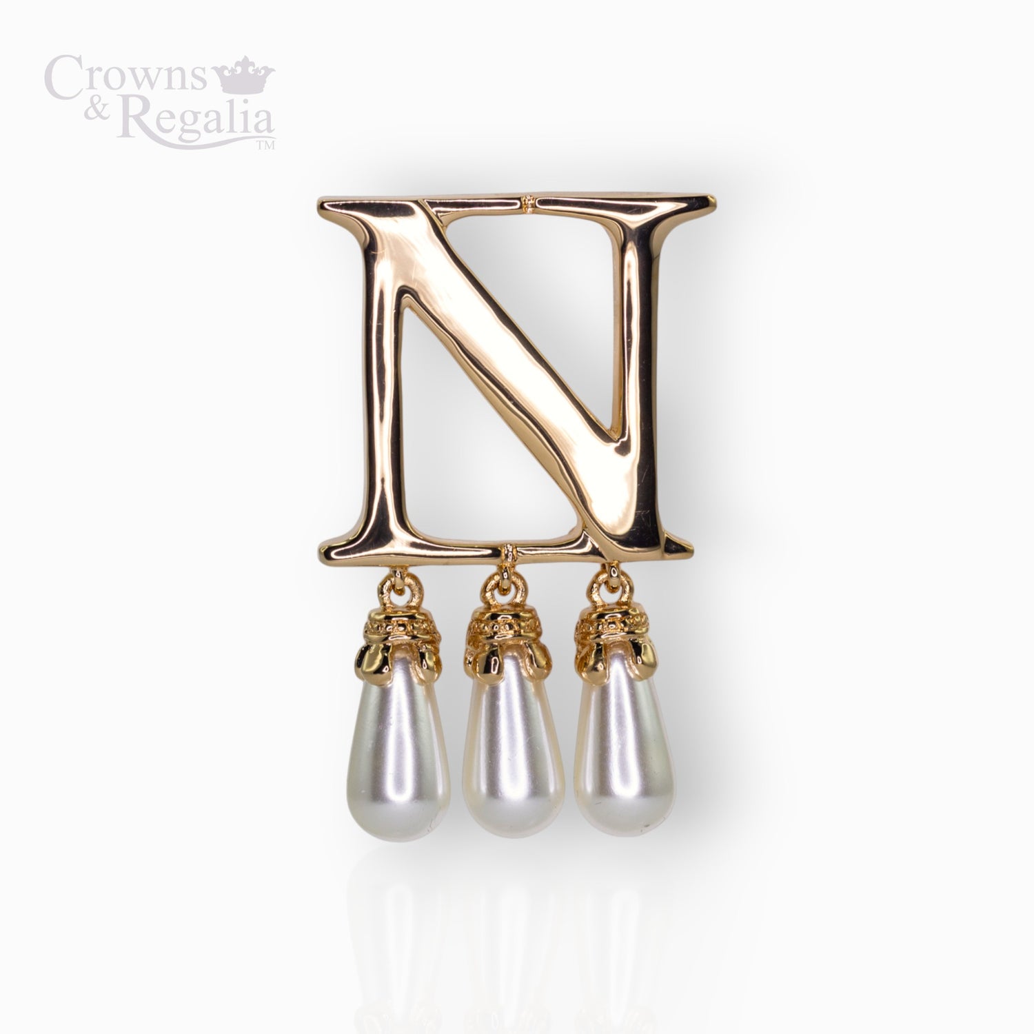 Gold brooch with letter 'N' and pearl-like droplets on a white background.