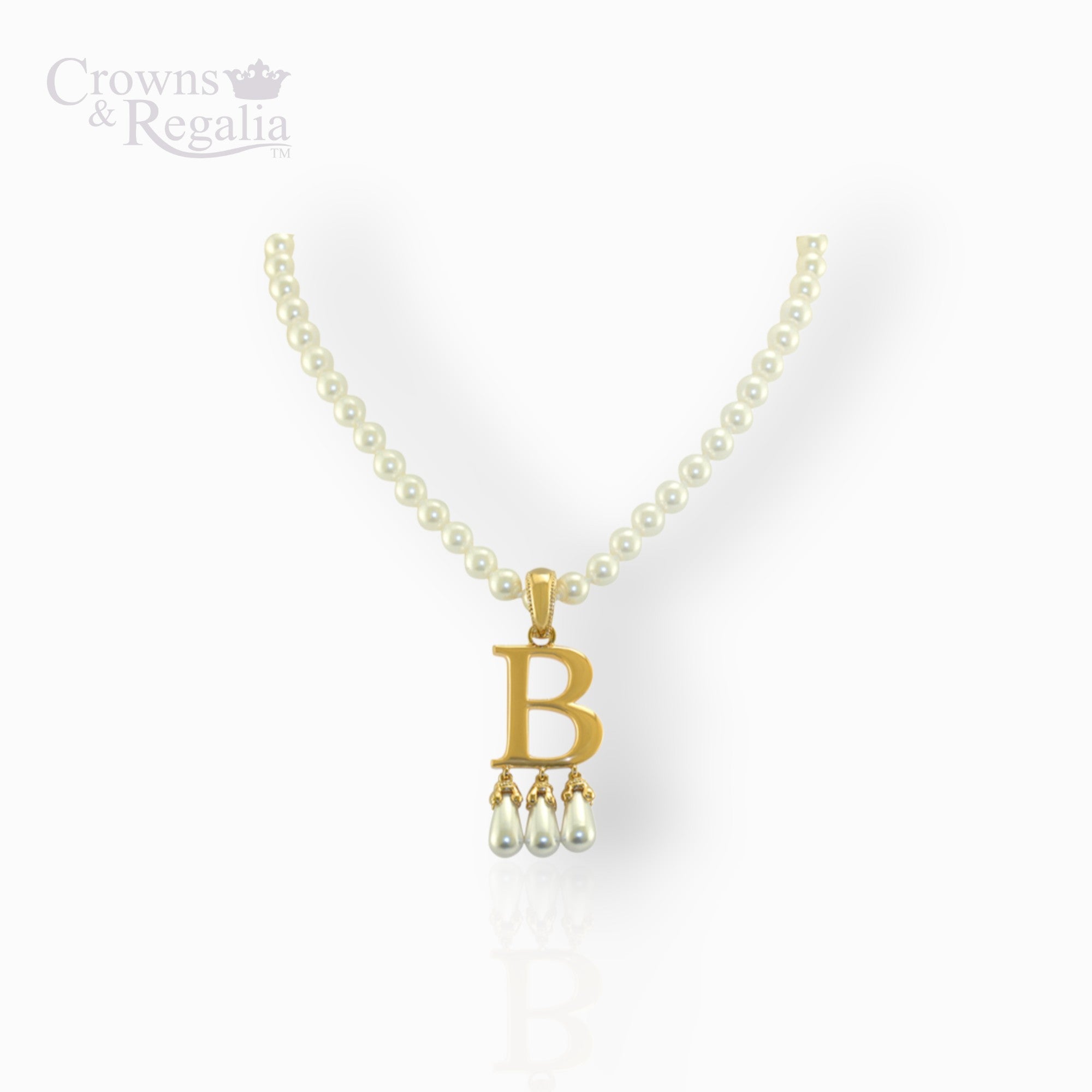 Gold necklace with 'B' pendant and pearl drops on a white background, branded 'Crowns & Regalia'.